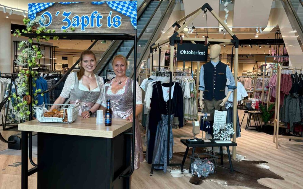 Zwei Mitarbeiterinnen in Trachten an einer kleinen Bar mit Bier und Laugengebäck