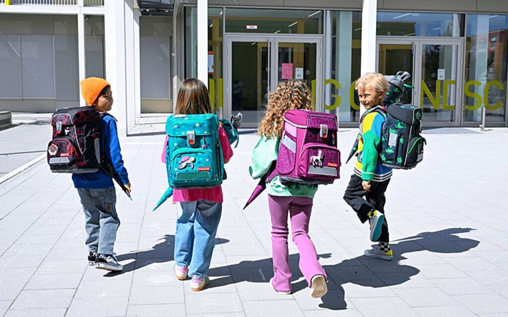 4 Schulkinder mit Ranzen gehen zur Schule