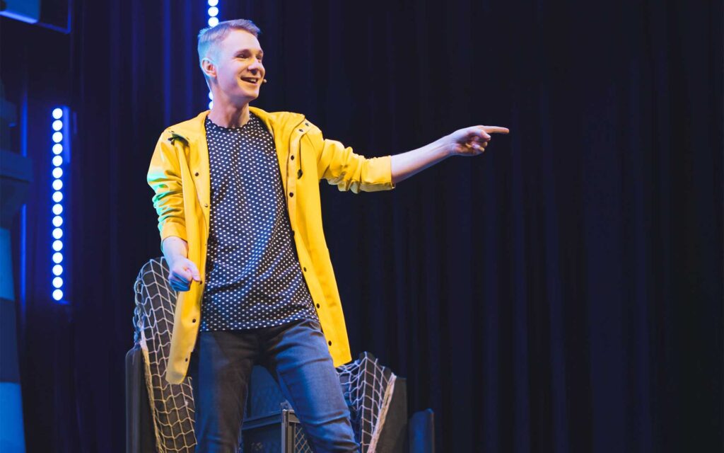 Comedian Till Frömmel in gelber Regenjacke auf der Bühne