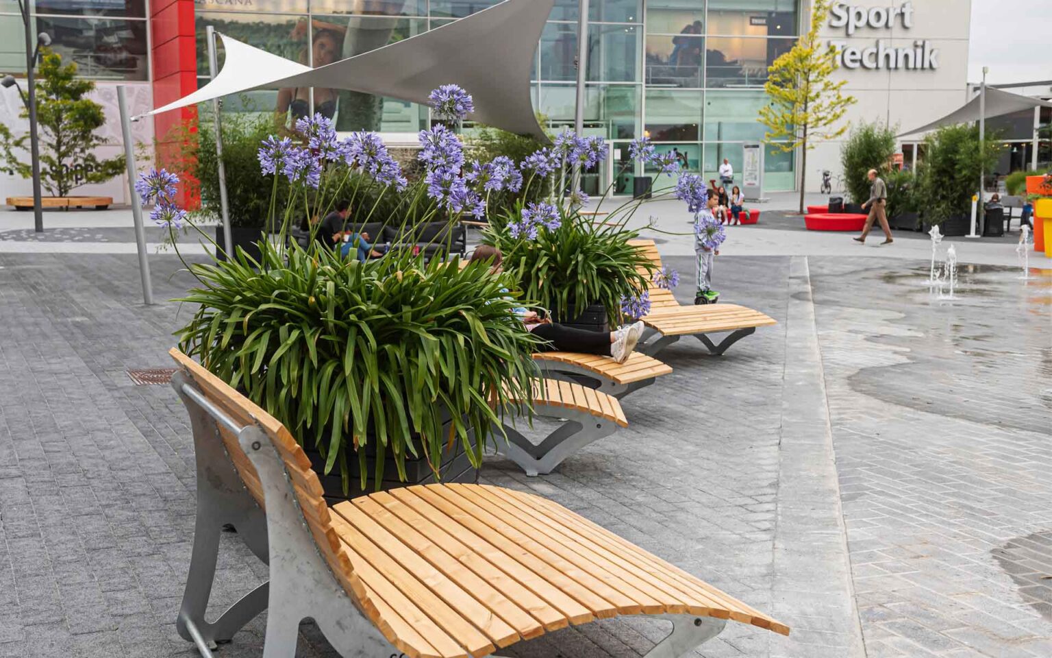 Holzliegen und Blumen am Brunnen auf dem Plaza