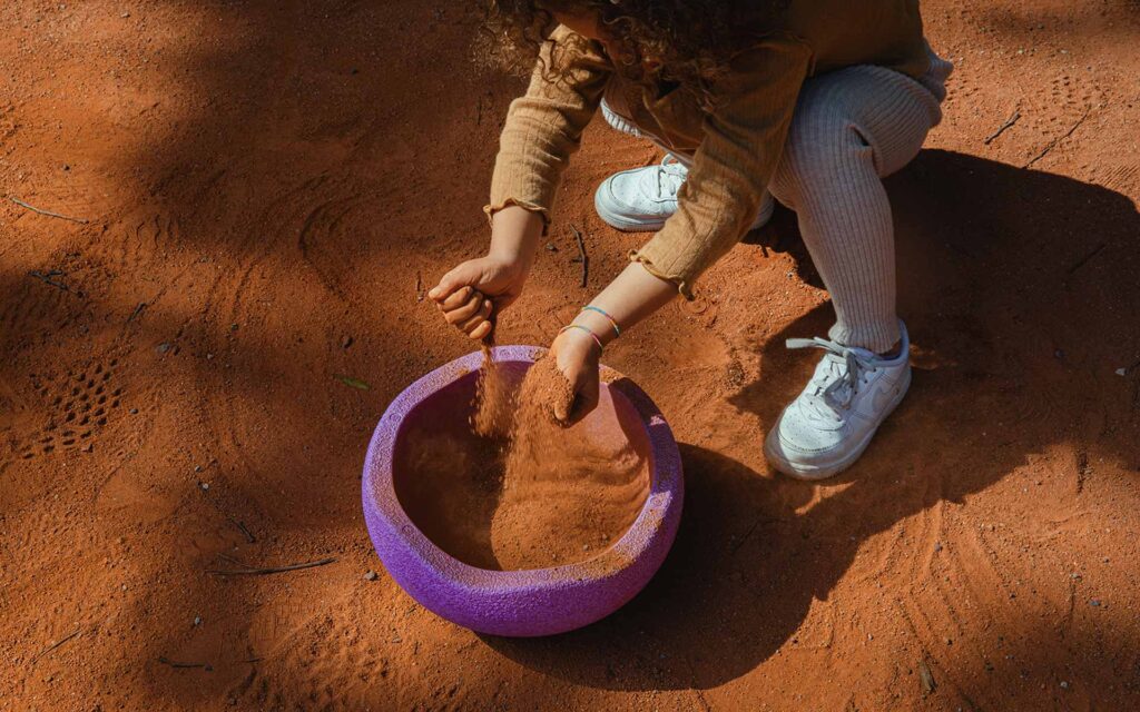 Kind spielt mit Stapelstein im Sand