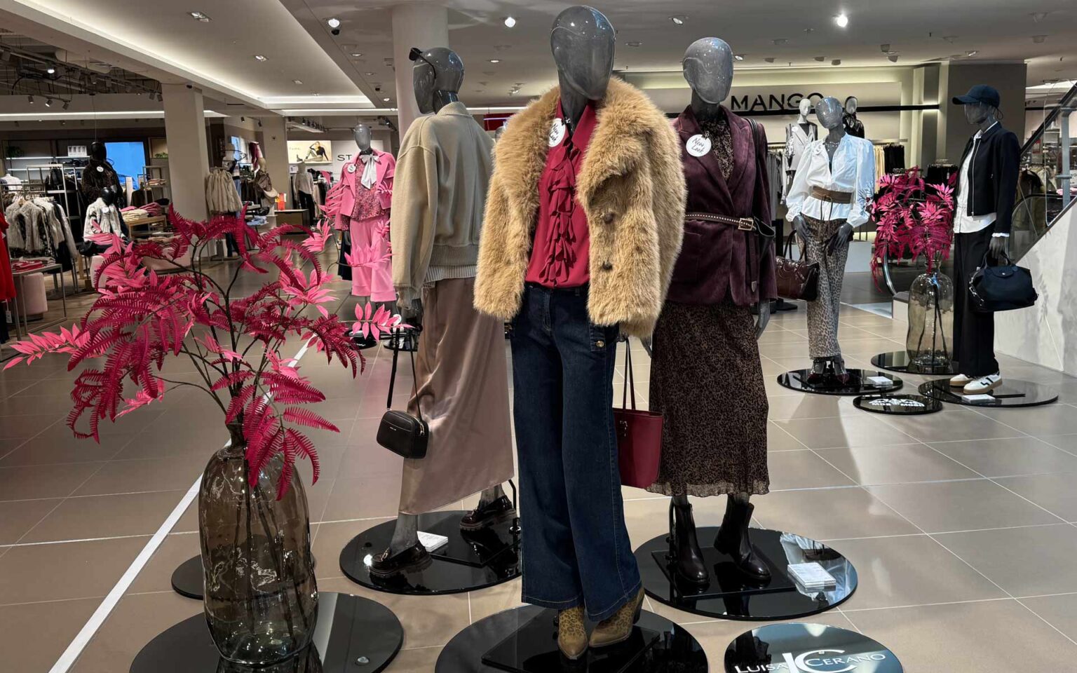 Highlightfläche an der Rolltreppe mit drei Puppen, welche herbstlich winterliche Outfits tragen in den Farben Rot, Beige, Rosa und Braun.