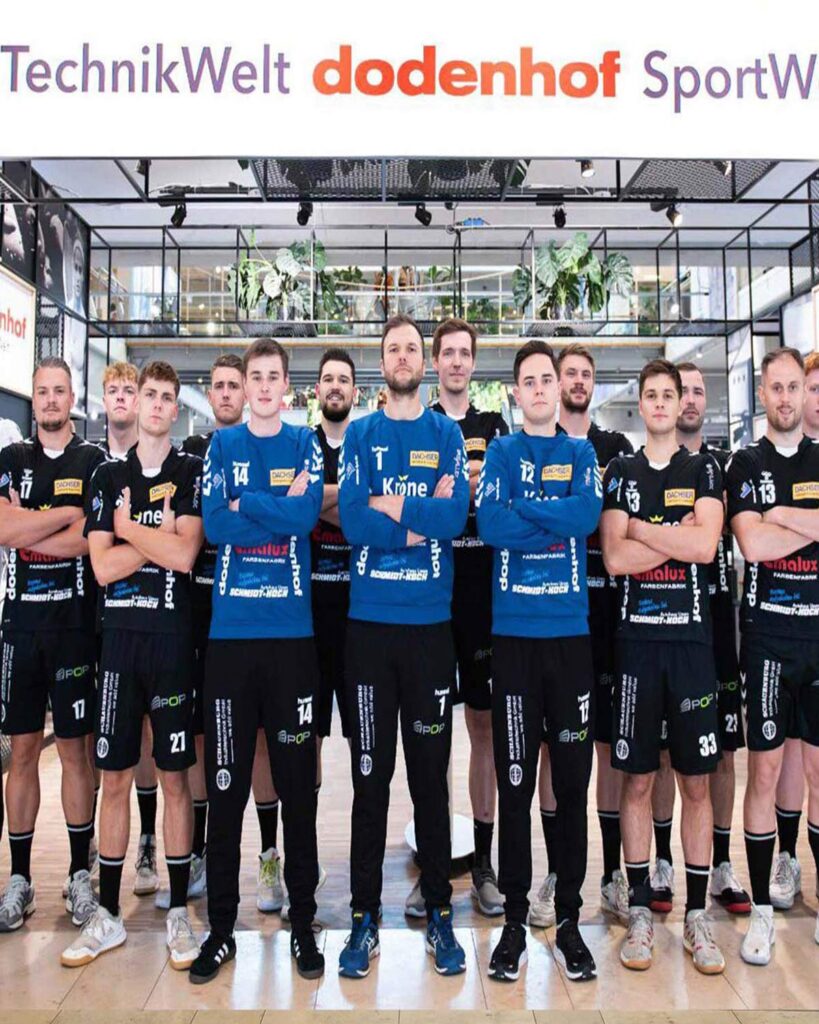 Handball Mannschaft posiert in schwarzer und blauer Kleidung vor der Sportwelt