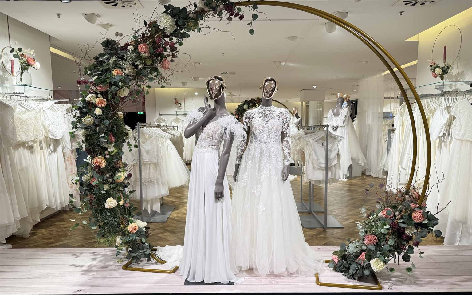 Zwei Figuren in Brautkleidern unter einem Blumenbogen im Brautsalon