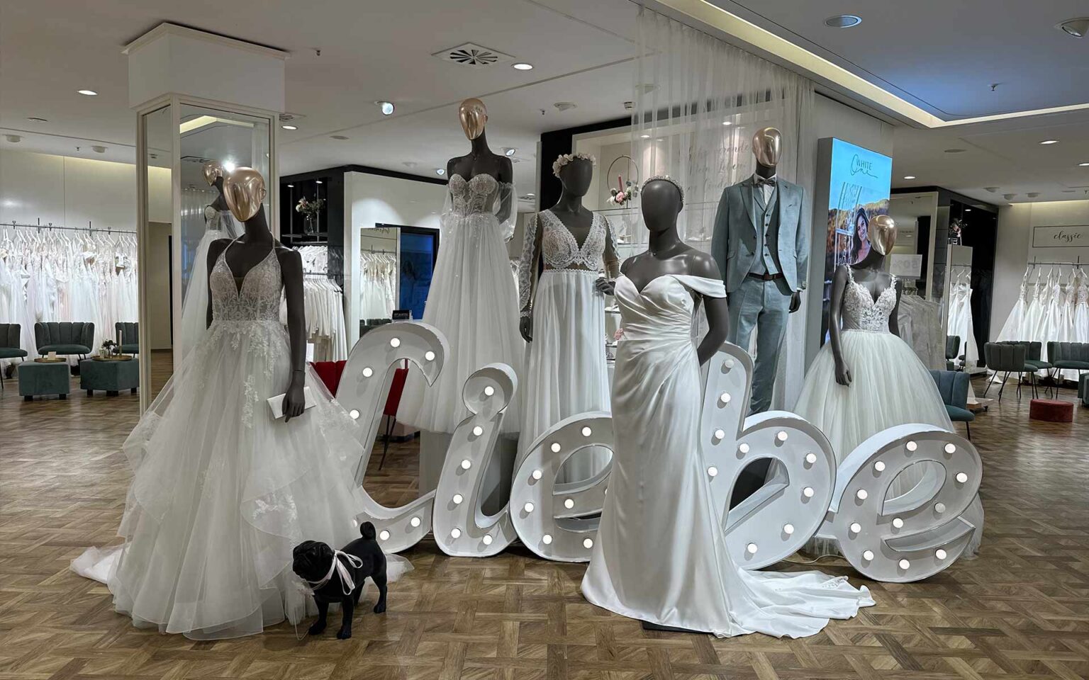 Mehrere Figuren in Brautmode vor dem Schild "Liebe" im Brautsaloneingang