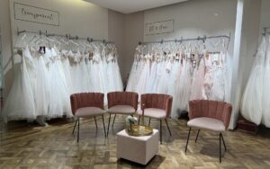 Brautkleider an Stangen in verschiedenen Stilen, davor Stühle in rosa