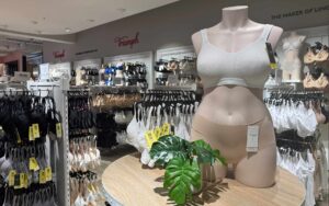 Figur im schlichten Dessous mit vielen BHs von Triumph im Hintergrund