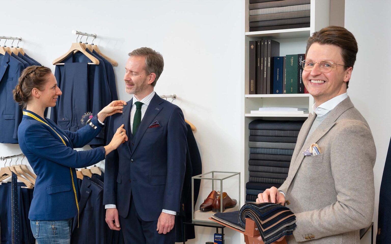 Anzug wird in der Maßkonfektion von einer Mitarbeiterin an einem Kunden abgesteckt