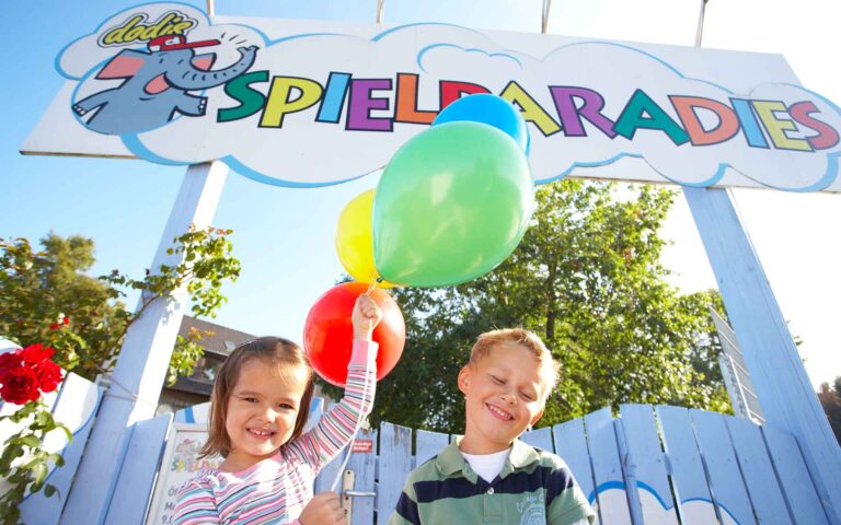 Schriftzug Spieleparadies mit zwei Kindern und Luftballons